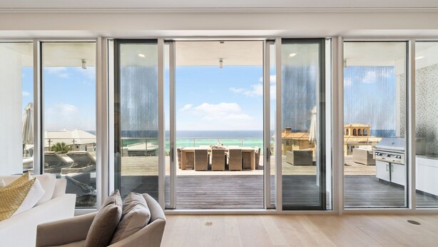 A modern living room with a large sliding glass door leading to an outdoor patio with a view of the ocean.