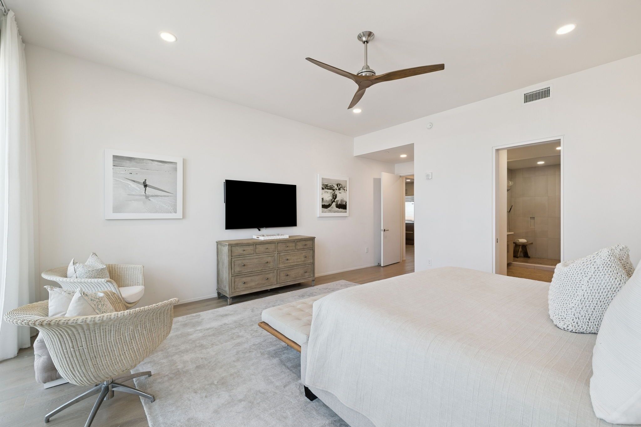 A spacious bedroom with a large bed, a ceiling fan, a flat-screen TV, and a modern dresser.