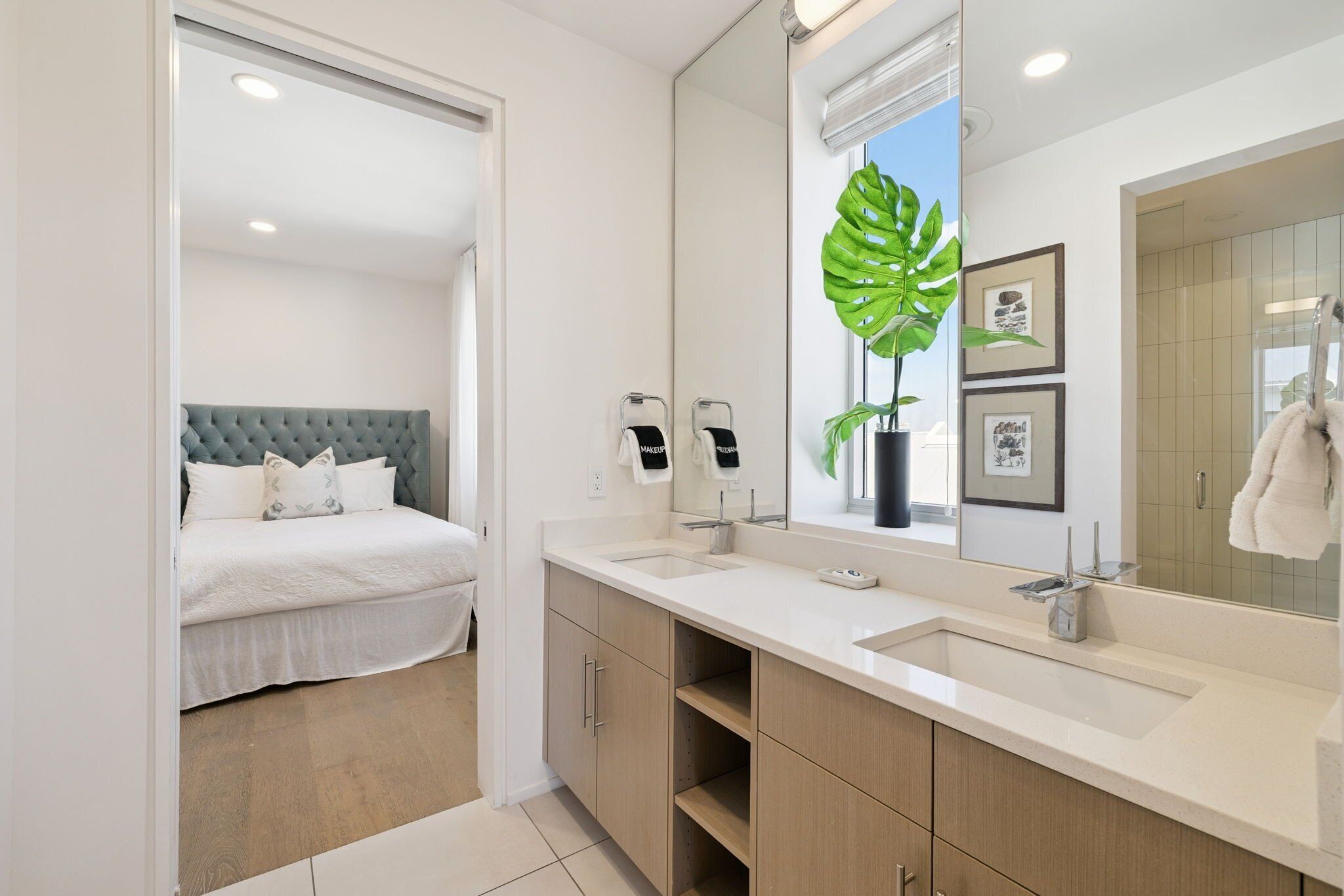A modern bathroom with a large mirror, two sinks, and a bed with a grey headboard.