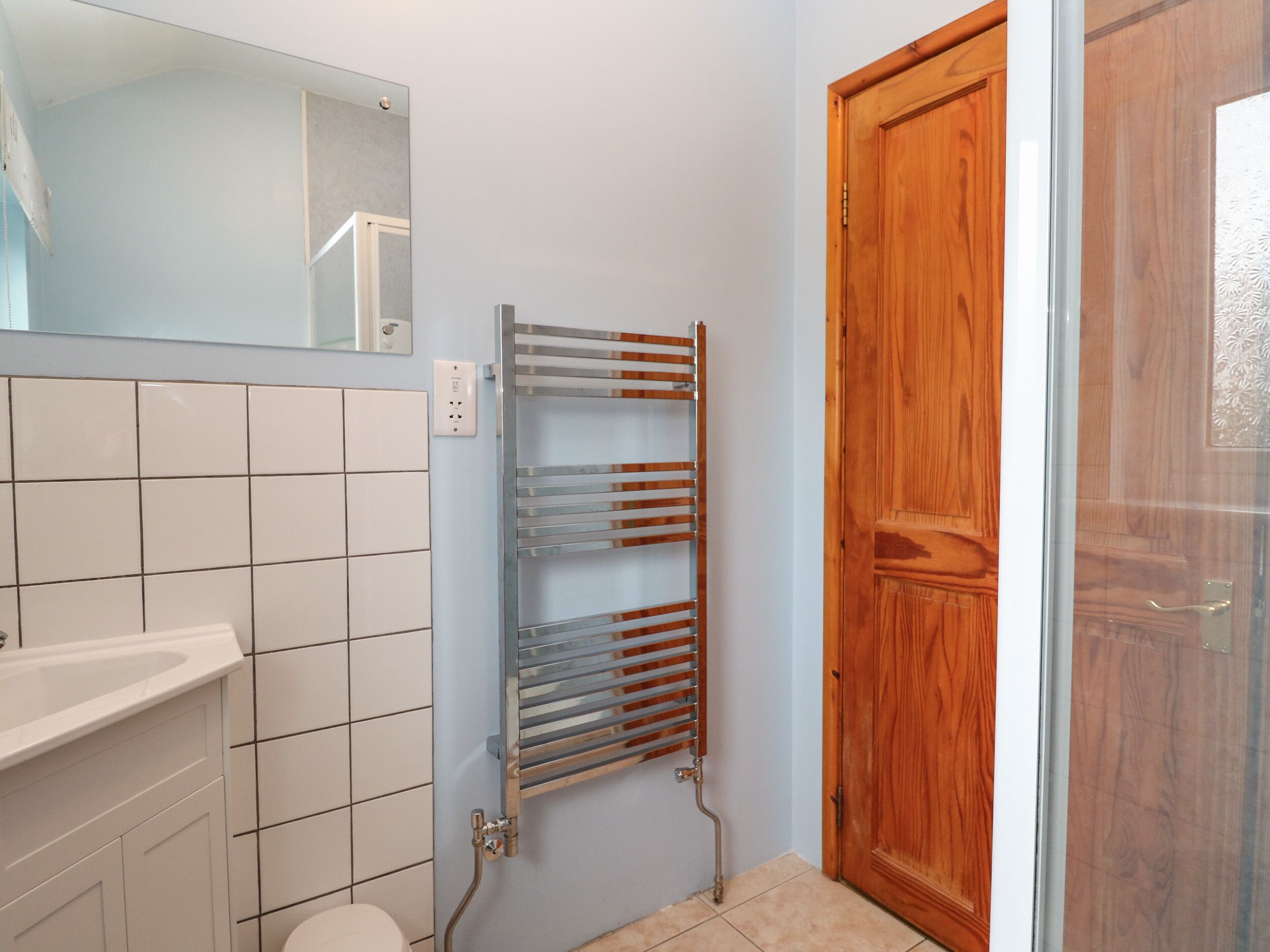 Une salle de bain avec un lavabo blanc, un miroir, un porte-serviettes et une porte en bois.