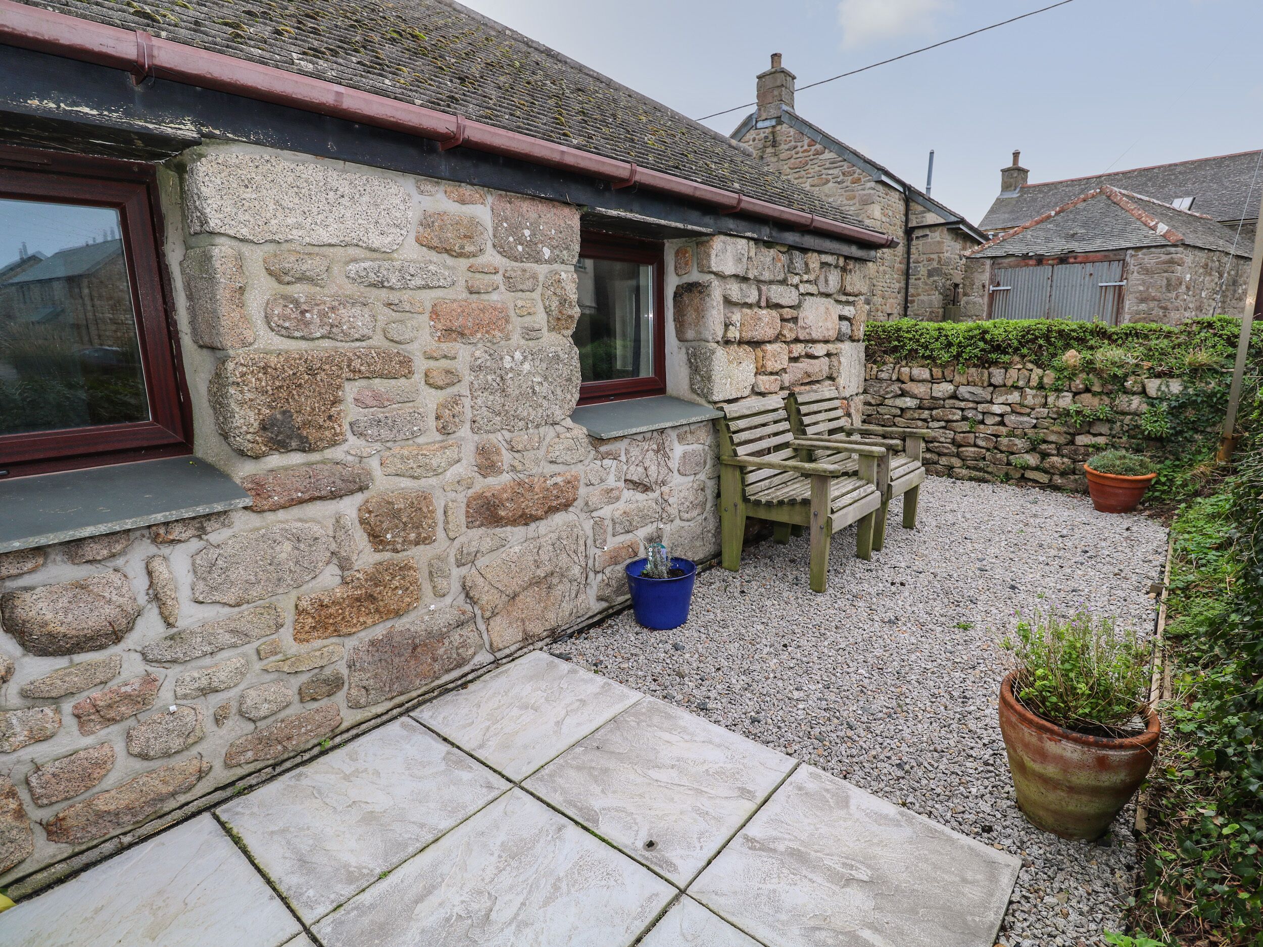 A stone house with a gravel patio, a wooden bench, and a potted plant.