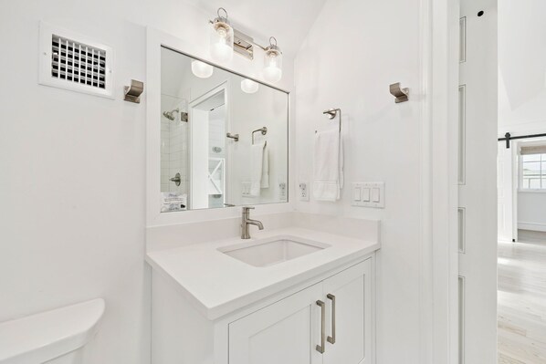 A modern bathroom with a white sink, mirror, and vanity, featuring a light fixture above the mirror.