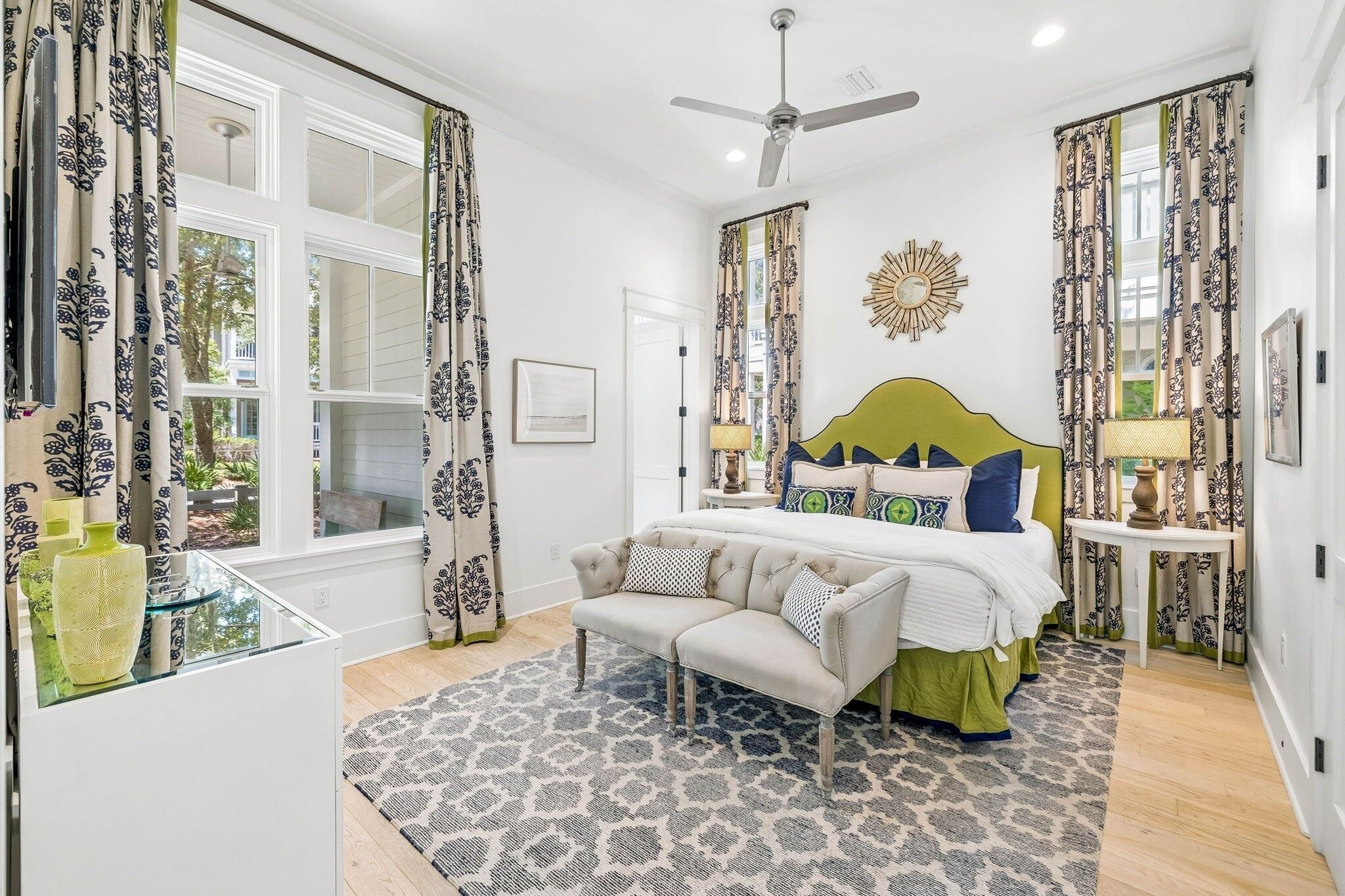 Une chambre à coucher comprenant un lit, un canapé, une table de chevet, une lampe, un ventilateur de plafond et des rideaux à motifs.