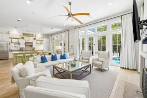 A spacious living room with a large window, a ceiling fan, and a view of a pool.