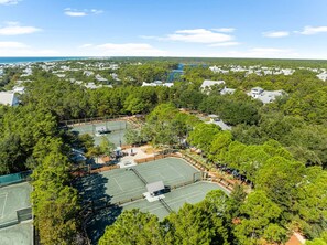 An aerial view of a residential area with multiple tennis courts surrounded by dense trees.