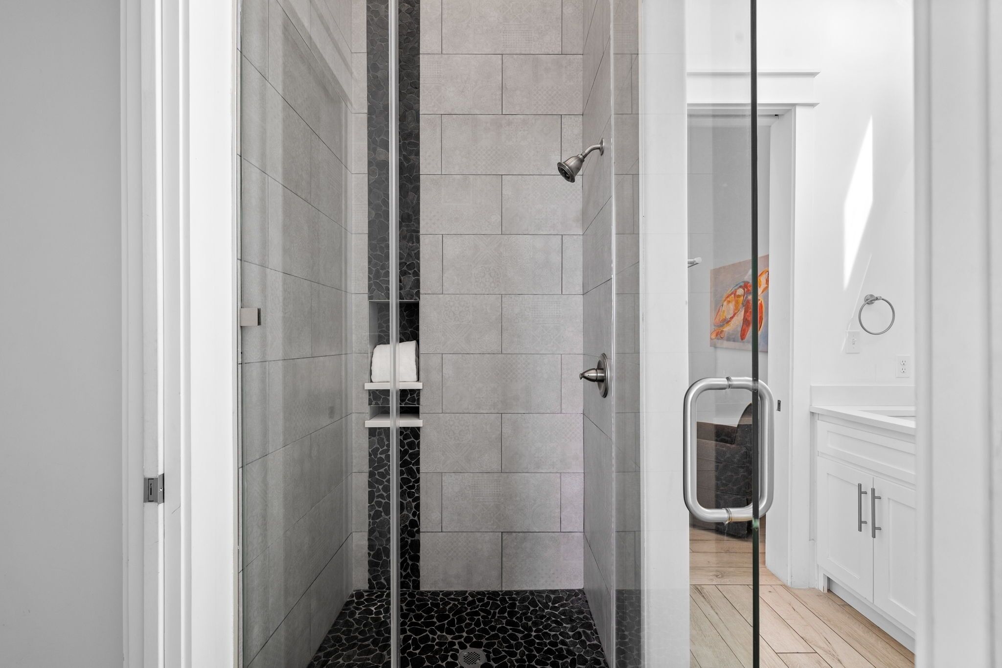 Une salle de bain moderne avec une douche à parois de verre, des murs recouverts de carreaux blancs et un plancher en bois.