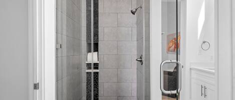 Une salle de bain moderne avec une douche à parois de verre, des murs recouverts de carreaux blancs et un plancher en bois.