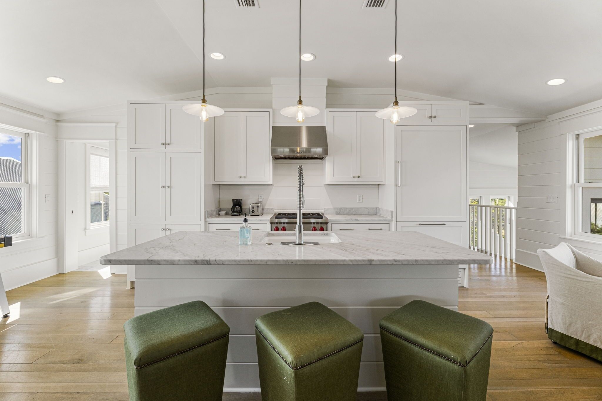 A spacious kitchen with white cabinetry, a central island with bar stools, pendant lighting, and a stainless steel range hood.