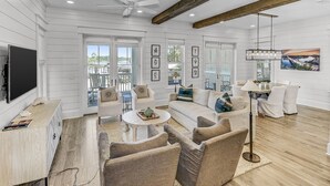 A spacious living room with a large TV, comfortable seating, and a ceiling fan.