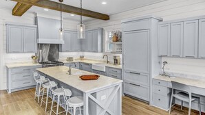 A modern kitchen with a central island, bar stools, and a built-in workstation.