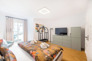 A modern bedroom with a large bed, a TV, a wardrobe, and a window with curtains. - "Meeresbrise" Luxury Apartment with Sauna & Ocean View | Terrace | Near the Beach | Dog-Friendly (Binz)