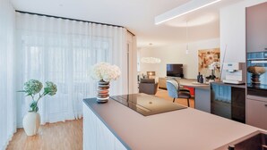Una cucina moderna con isola centrale, un'area pranzo con una sedia e un soggiorno con televisore e opere d'arte.