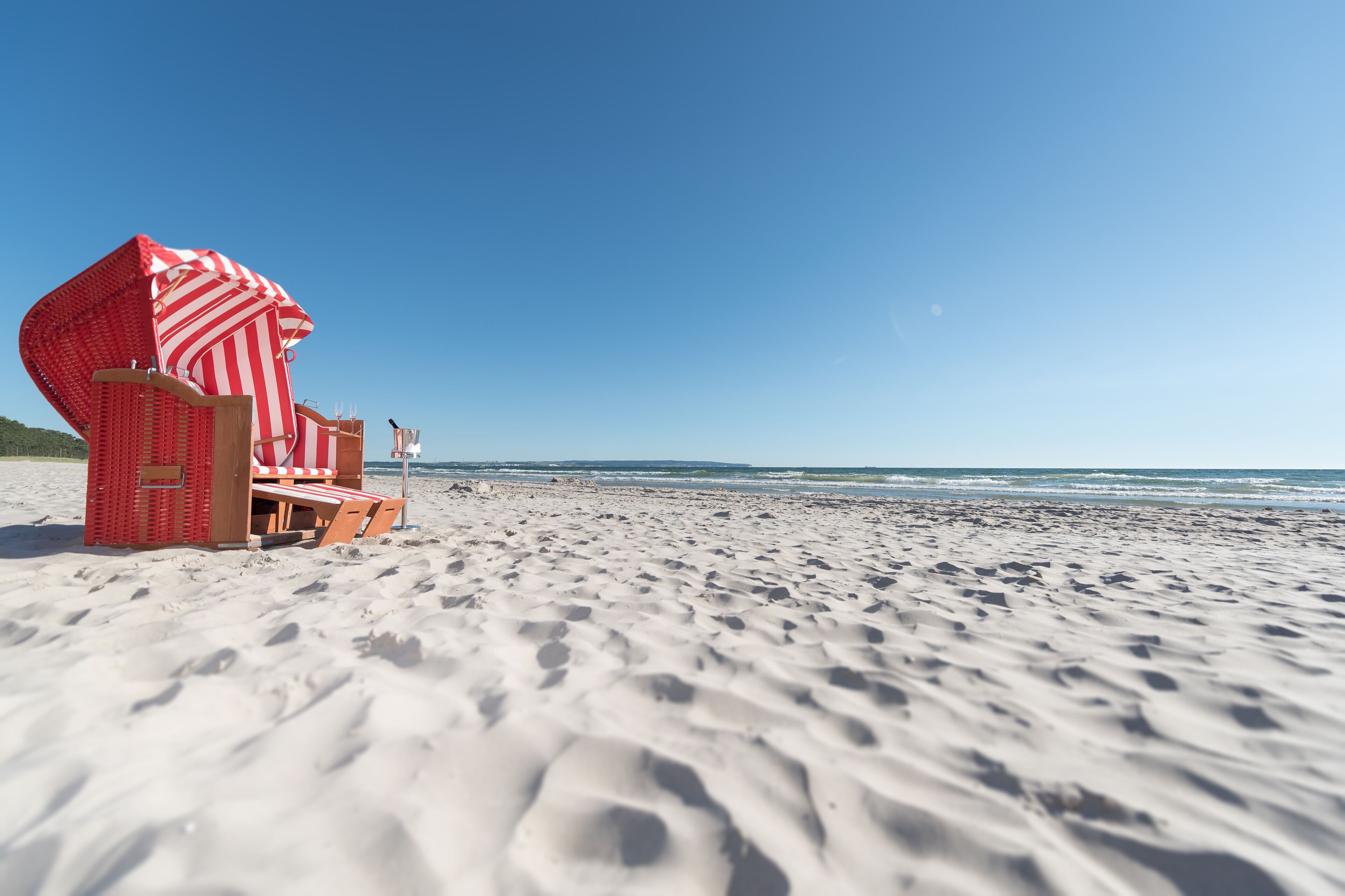 A beach with a red and white striped beach chair and a wooden lounge chair.