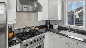 A modern kitchen with white cabinets, a stainless steel range hood, a gas stove, and a window with a view of a house. - amazing Gulf Views 420b Watersound Crossings 3br, Corner Unit 3 Bedroom Condo by RedAwning (Santa Rosa Beach)