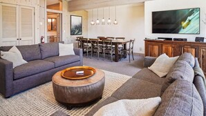 A modern living room with a gray sofa, a round coffee table, and a dining area with a wooden table and chairs. - Serene Forest-Front Retreat: 4BR Rocky Ridge Gem (Tahoe City)