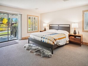 A bedroom with a bed, nightstands, a lamp, a view of the outdoors, and a sliding glass door.