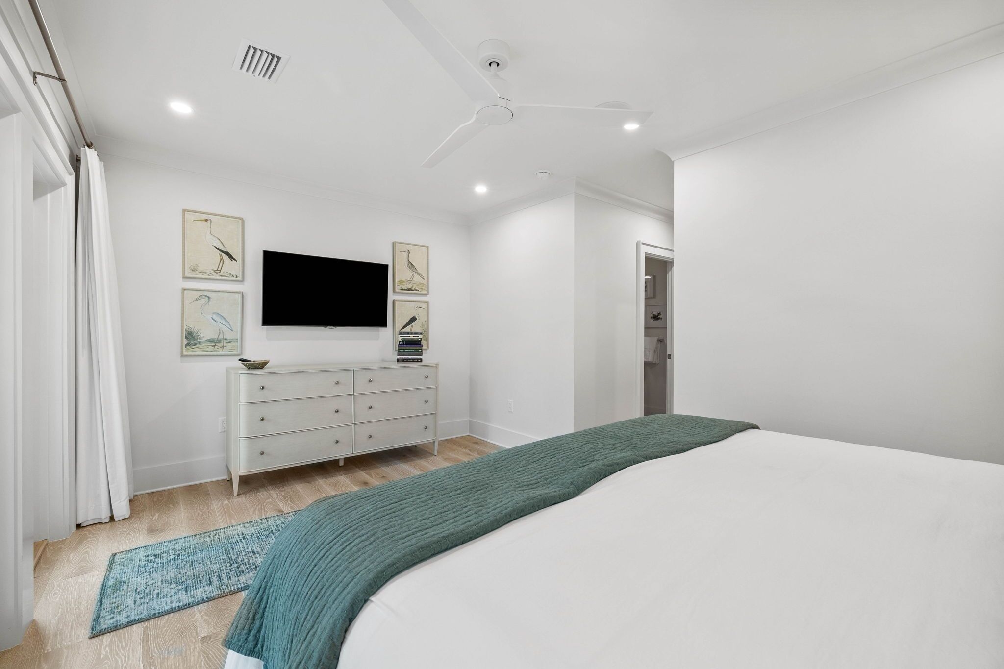 A modern bedroom with a bed, a dresser, and a flat-screen TV mounted on the wall.