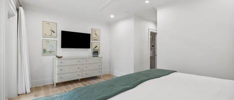A modern bedroom with a bed, a dresser, and a flat-screen TV mounted on the wall.