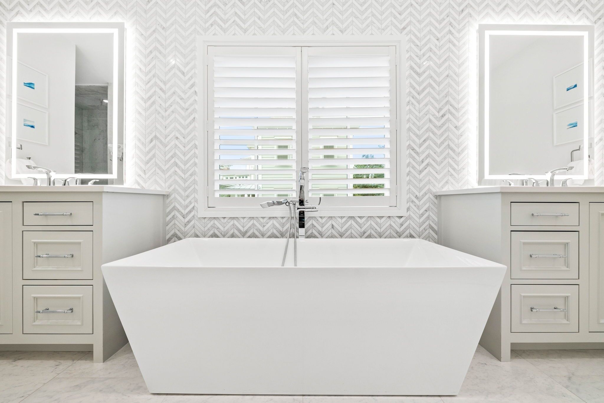 A modern bathroom with a freestanding bathtub, two vanity mirrors, and a window with blinds.