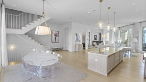 A spacious, modern kitchen with a central island, a dining area with a round table and chairs, and a staircase leading to an upper level. - Private Pool, Gulf Views + Luxurious Features Throughout This Lovely Residence 6 Bedroom Condo by RedAwning (Panama City Beach)