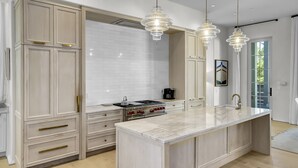A modern kitchen with a large island, white cabinetry, and pendant lighting. - Private Pool, Gulf Views + Luxurious Features Throughout This Lovely Residence 6 Bedroom Condo by RedAwning (Panama City Beach)