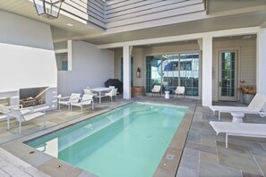 Un espace piscine extérieur moderne, doté de chaises longues, d’un barbecue et d’une table à manger.
