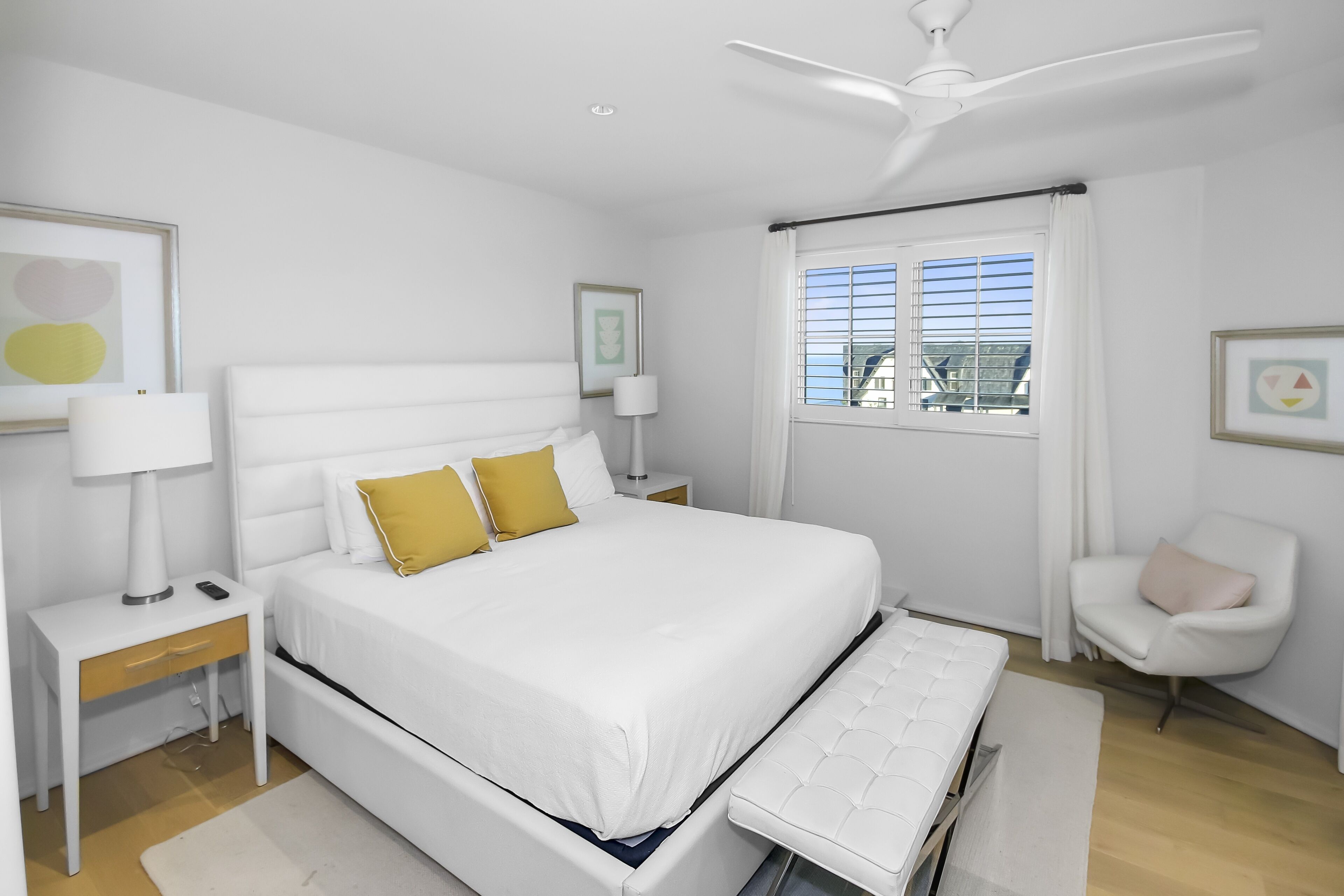 Un dormitorio moderno con una cama blanca, una mesita de noche, una silla y una ventana con persianas.