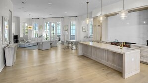 A spacious living area with a large island, a dining table, and a kitchen area with a modern stove and pendant lights. - Private Pool, Gulf Views + Luxurious Features Throughout This Lovely Residence 6 Bedroom Condo by RedAwning (Panama City Beach)