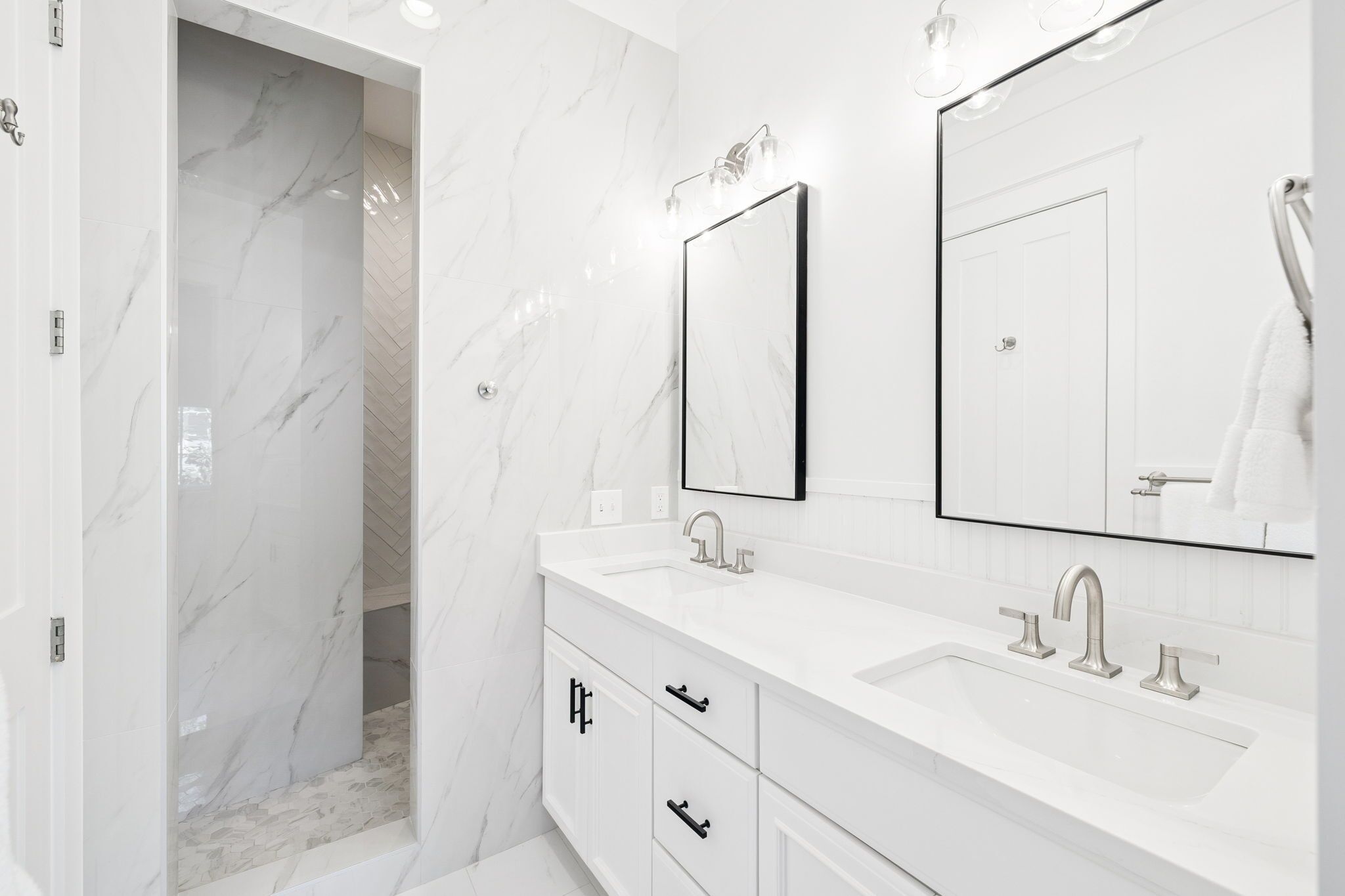 Un baño moderno con pared de mármol blanco, tocador doble y un espejo grande.