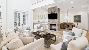 A spacious living room with a fireplace, white furniture, and a high ceiling. - Golf Cart, Close To The Sand Hill Pool, Great Outdoor Space Lake District, Watercolor Home 5 Bedroom Home by RedAwning (Santa Rosa Beach)