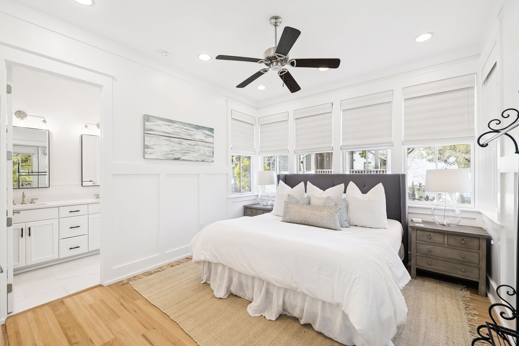 A bedroom with a bed, nightstands, a ceiling fan, and large windows.