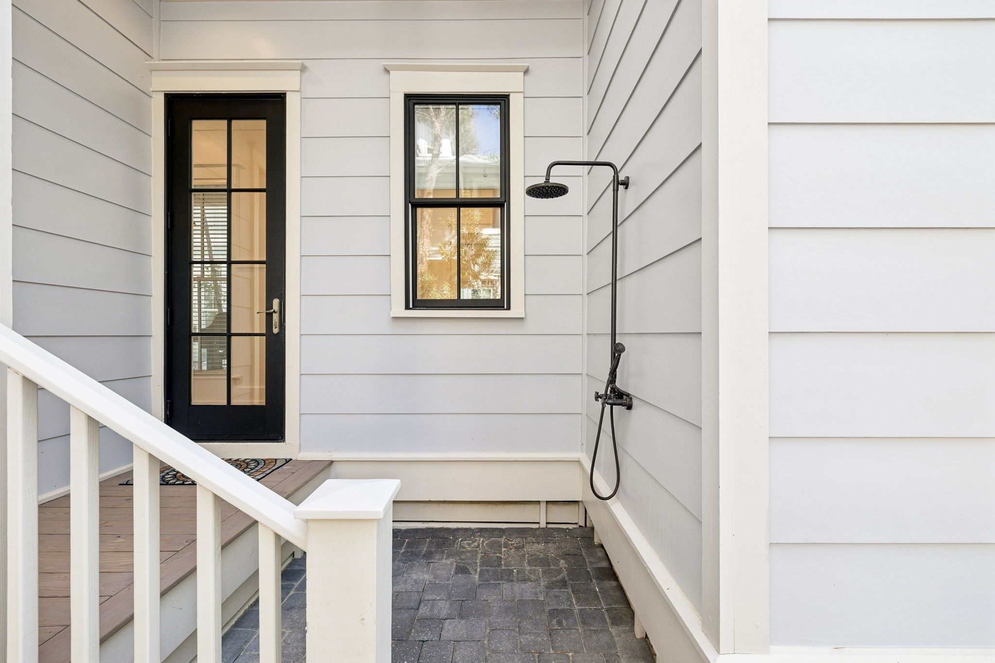 A covered outdoor area with a black door, a window, and a showerhead.