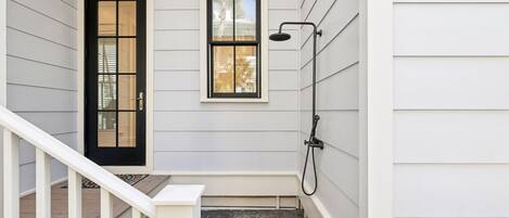 A covered outdoor area with a black door, a window, and a showerhead.