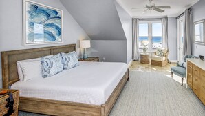 Ein Schlafzimmer mit einem großen Bett, einem Deckenventilator, Blick auf den Strand und einer hölzernen Kommode.