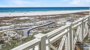 Blick auf einen Strand vom Balkon mit weißer Reling, ein sandiger Strand und ein klarer, blauer Himmel.