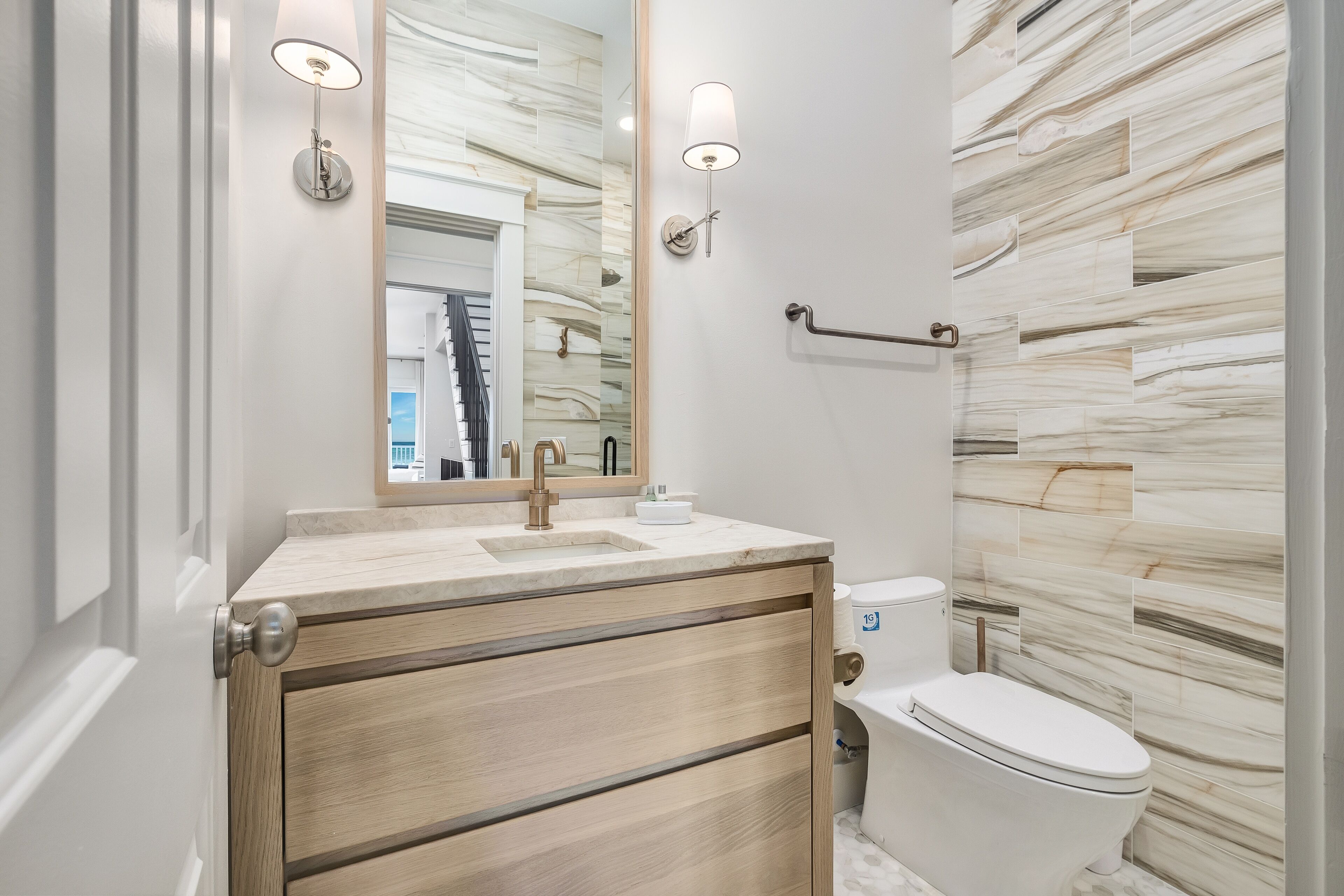 A modern bathroom with a marble backsplash, a sink with a mirror, and a toilet.