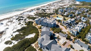 An aerial view of a coastal residential area with beachfront properties, a large building with multiple floors, and a swimming pool. - GULF VIEWS from ALL Bedrooms! 308 Compass Point 1 in WaterSound Short walk to the beach and pool 3 Condo by RedAwning (Santa Rosa Beach)