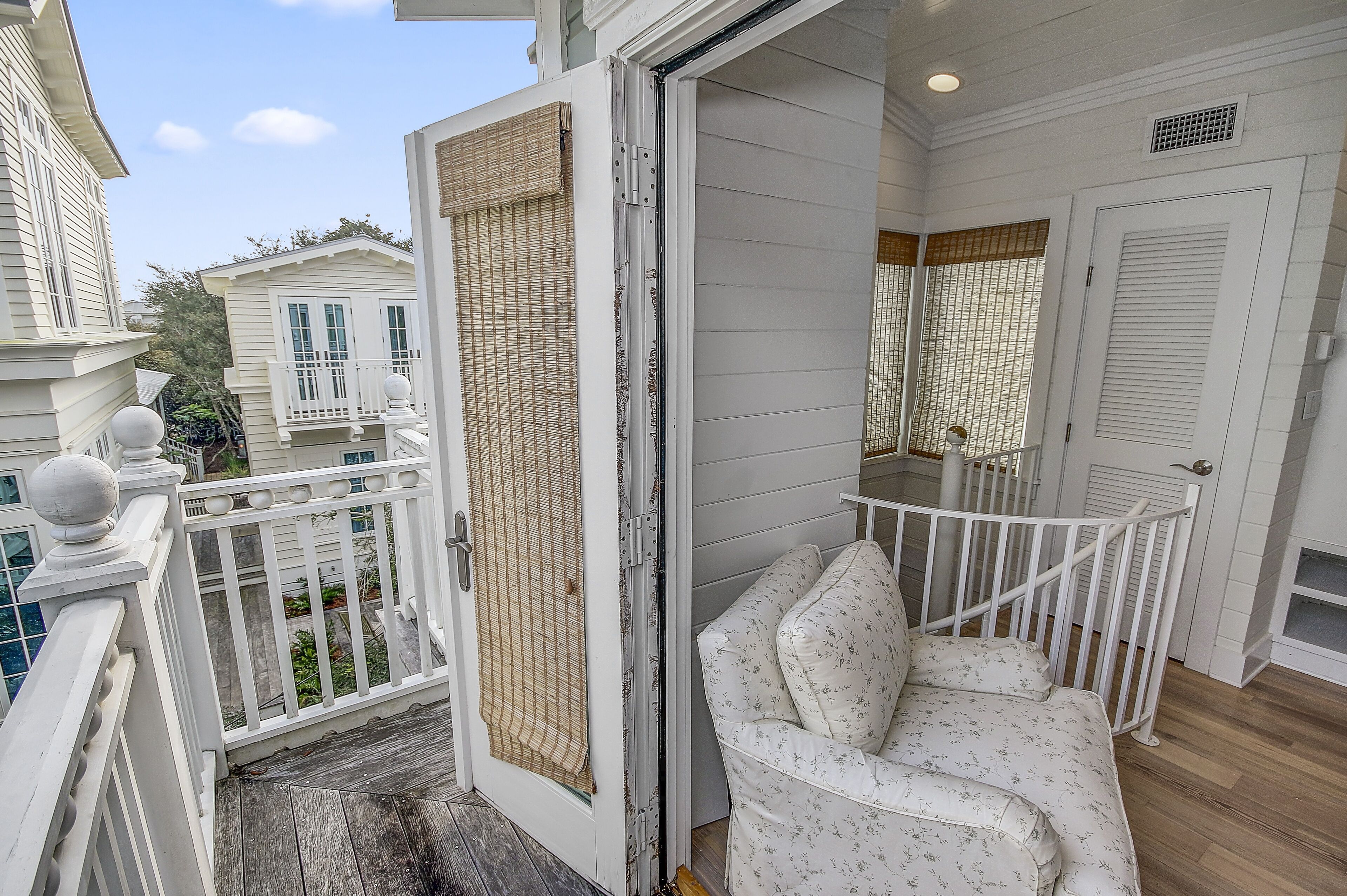 A balcony with a white railing, a white cushioned bench, and a door leading to an interior space.