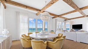 A spacious room with a round table and yellow chairs, large windows with a view, and a white sofa.