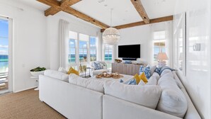 A modern living room with a large white sectional sofa, a chandelier, and a view of the sea.