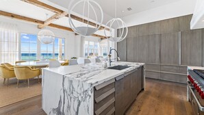 A modern kitchen with a marble island, wooden beams, and pendant lighting.