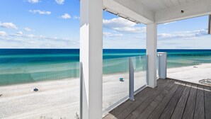 A beach view from a covered wooden deck with a clear sky and turquoise ocean.