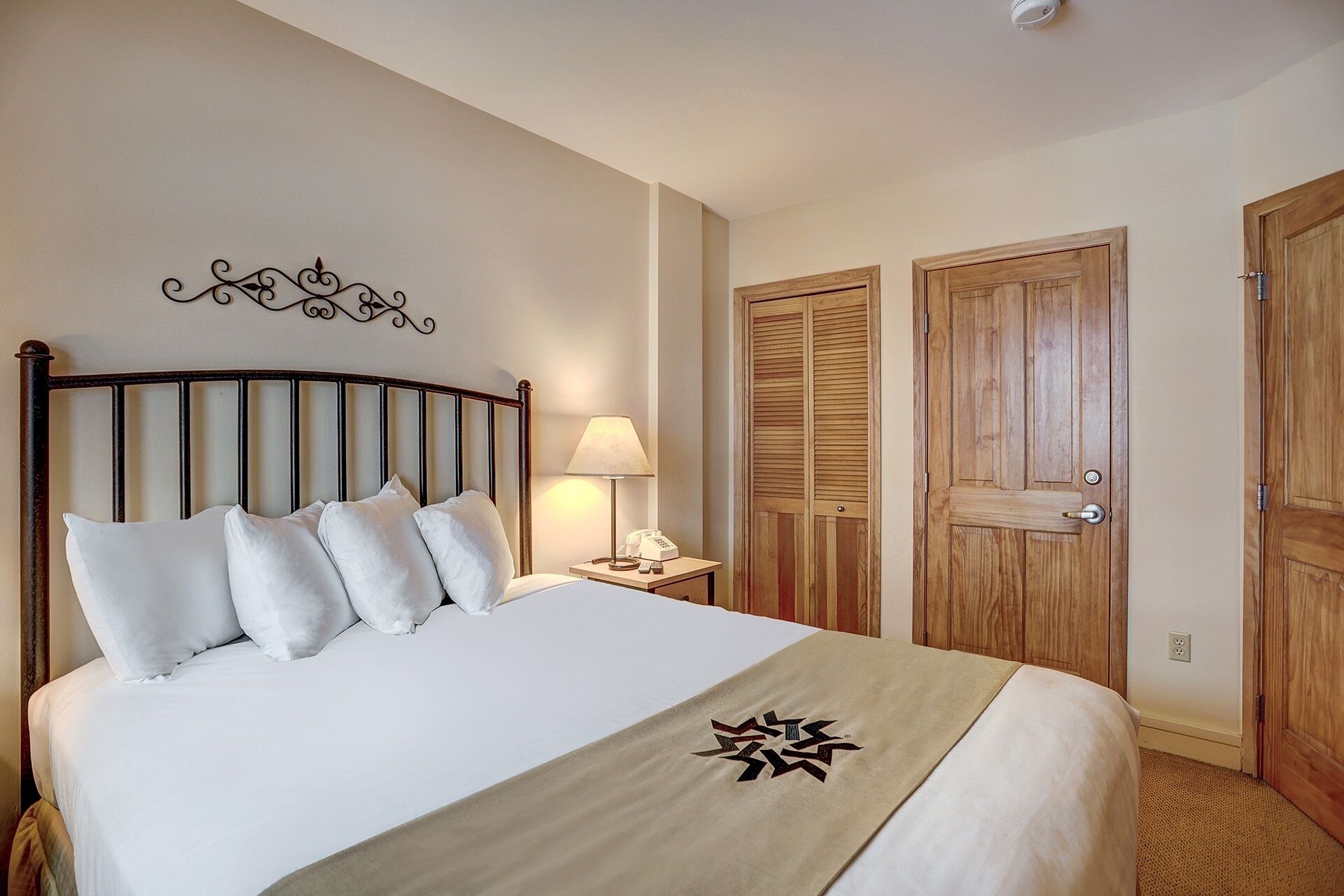 A neatly made bed with white linens and a decorative headboard, a bedside lamp, and a wooden door with a handle.