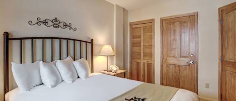 A neatly made bed with white linens and a decorative headboard, a bedside lamp, and a wooden door with a handle.