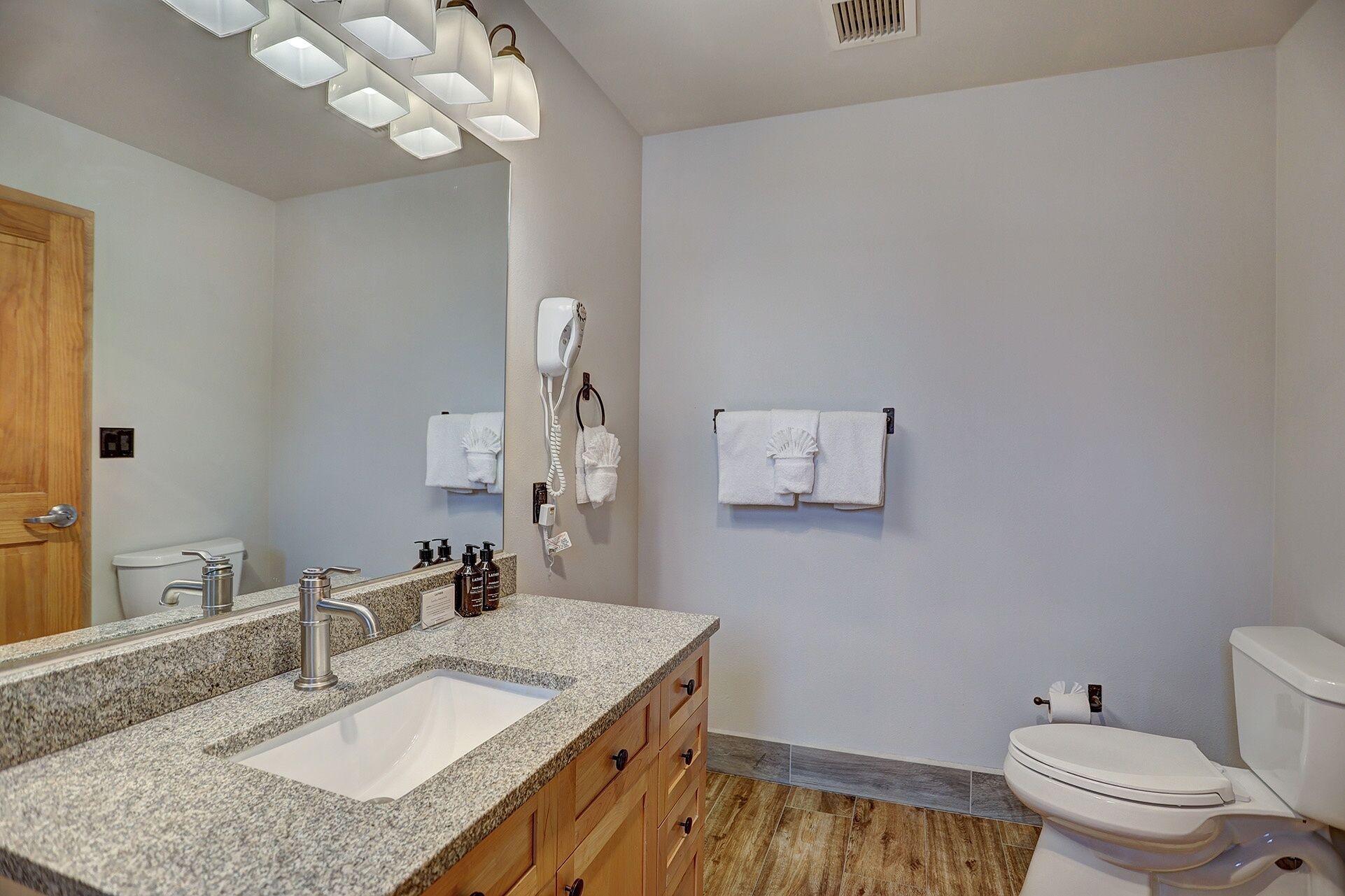 A bathroom with a granite countertop sink, wooden cabinets, a white toilet, and a towel rack with two towels.