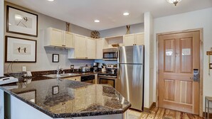 A modern kitchen with granite countertops, stainless steel appliances, and light wood cabinetry.