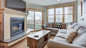 A cozy living room with a fireplace, a sofa set, and large windows offering a view of the outside.