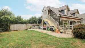 Ein zweigeschossiges Haus mit einer überdachten Terrasse, einem Holzzaun und einem gepflegten Rasen.