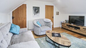 Ein Wohnzimmer mit grauem Sofa, einem gesteppten Sessel, einem Holztisch, einem Flachbildfernseher und einer Heizung.
