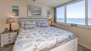 Un dormitorio con una cama grande, un ventilador de techo y vista al océano a través de una ventana.